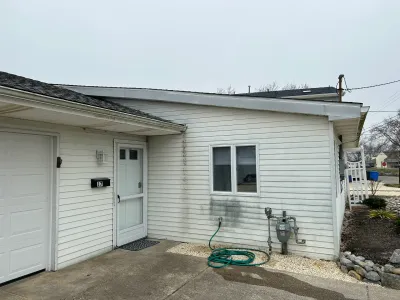 Side view of a house with vinyl siding showing dark staining below the roofline, garage, and entry door.