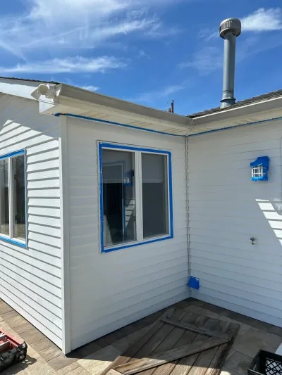 Corner of a house with new white vinyl siding and blue painter's tape around windows and trim.