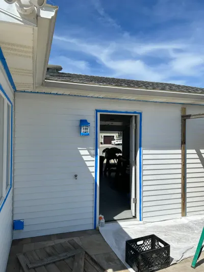 Exterior wall of a house with blue painter's tape around a door and light fixture, mid-paint prep.