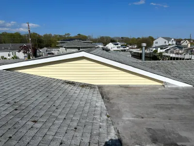 View from a rooftop showing shingled and flat roof sections with a yellow-sided gable, overlooking a waterfront neighborhood.