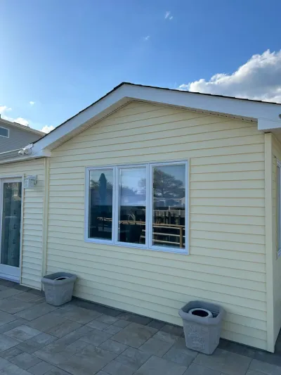 Yellow vinyl-sided house exterior with a triple window, paver patio, and clear blue sky.