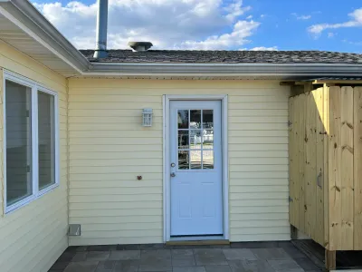 Side entrance of a yellow-sided home with a white glass-panel door and new wood fence enclosure.