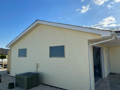Side view of a yellow vinyl-sided house with a gable roof, small windows, and an open sliding door.