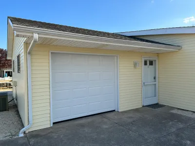 Side view of a yellow-sided home showing a white garage door and an adjacent entry door with a storm door.