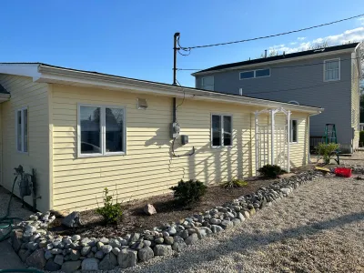 Side view of a yellow-sided ranch home with a new stone border garden bed and white trellis archway.