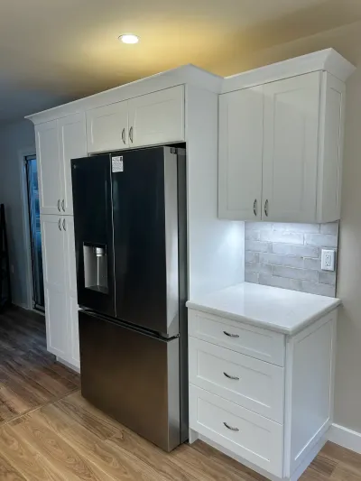 White shaker cabinets surround a stainless steel refrigerator with a gray tile backsplash nearby.