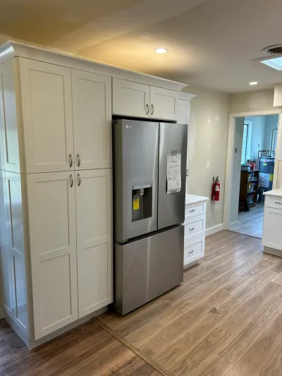White shaker cabinets surround a stainless steel refrigerator in a newly finished kitchen with wood-look flooring.