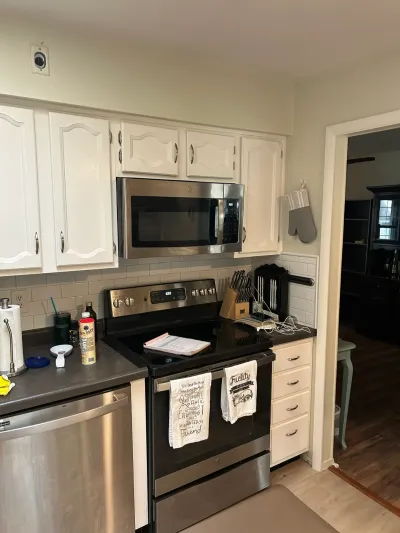 A white cabinet kitchen with stainless steel appliances and subway tile backsplash, opening to another room.