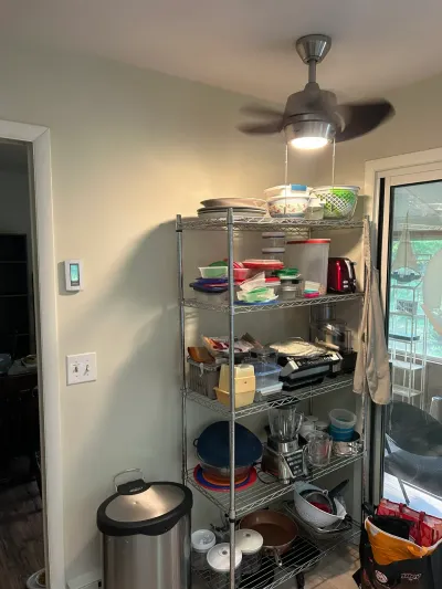 Kitchen corner with a wire shelving unit full of kitchenware, a trash can, and a sliding door to the porch.