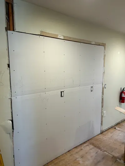 Newly installed drywall panels with visible seams and framing exposed along the edges of an under-construction wall.