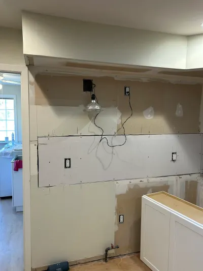 Kitchen wall mid-renovation with patched drywall, exposed wiring, and a newly installed white shaker cabinet.
