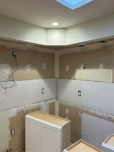 A kitchen under construction with unfinished drywall, a skylight, and new white cabinet boxes installed in the corner.