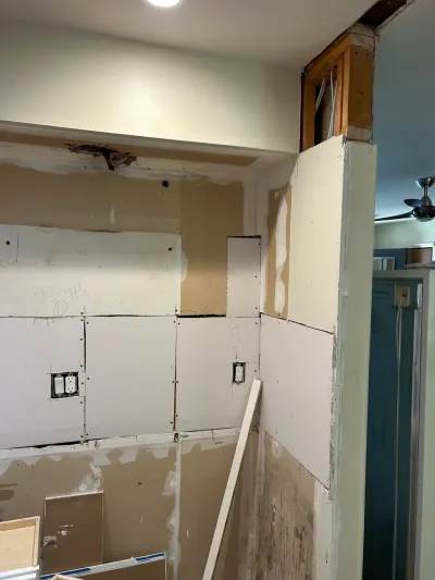 Kitchen wall mid-renovation showing unfinished drywall, exposed framing above a doorway, and visible wiring.