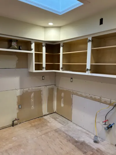 Kitchen mid-renovation with white upper cabinets installed but unfinished drywall walls and no countertops or lower cabinets