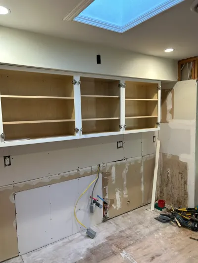 Kitchen renovation in progress with open upper cabinets, exposed plumbing, and unfinished walls under a skylight.