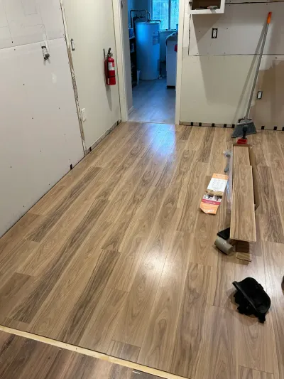 Basement under renovation with new plank flooring installed and unfinished drywall walls.