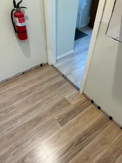 New wood-look vinyl plank flooring installed up to a doorway transition strip, with a fire extinguisher on the wall.