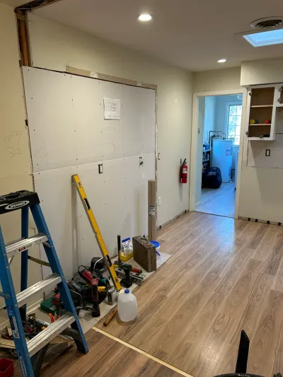 Kitchen mid-renovation with fresh drywall, new flooring, tools, and a view into a utility room with a water heater.