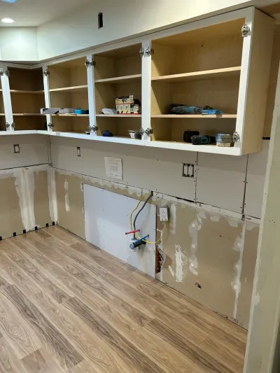 Kitchen mid-renovation with new upper cabinets installed but lower cabinets and wall finishing still incomplete.