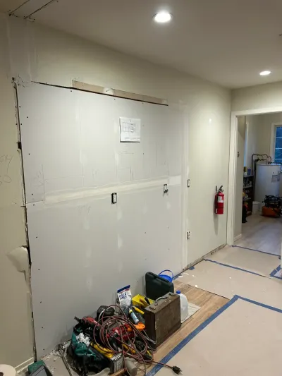 An unfinished drywall wall with exposed seams and tools scattered on a partially protected floor during renovation.