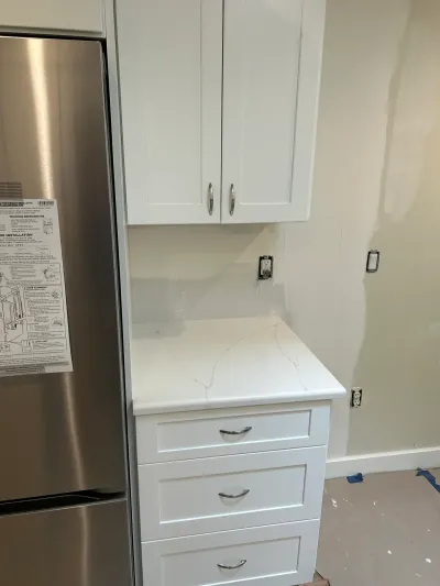 A kitchen mid-renovation with new white shaker cabinets, quartz counter, and a refrigerator with instructions still attached.