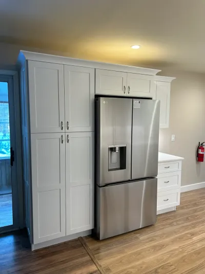 A finished kitchen with tall gray shaker cabinets surrounding a stainless steel refrigerator and wood-look flooring.