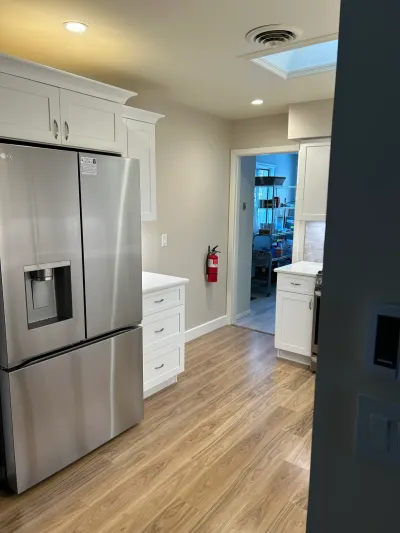 Finished kitchen with white shaker cabinets, quartz counters, stainless fridge, and wood-look vinyl flooring.