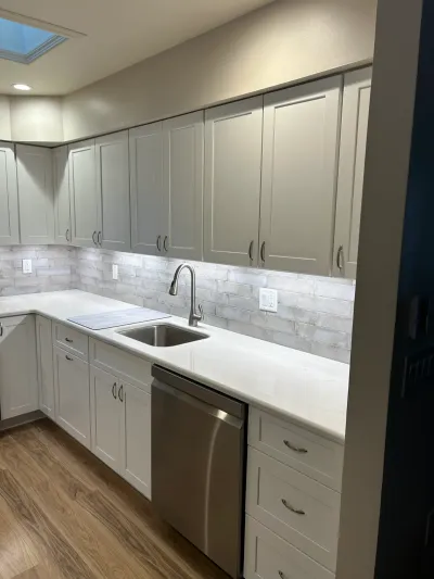 Finished kitchen with gray shaker cabinets, white quartz counters, subway tile backsplash, and wood-look flooring.