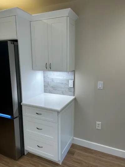 White shaker cabinets with quartz counter, gray subway tile backsplash, and under-cabinet lighting beside a stainless fridge.