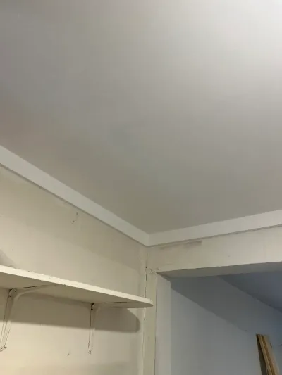 Close-up of white crown molding and a shelf bracket in the corner of a basement room.