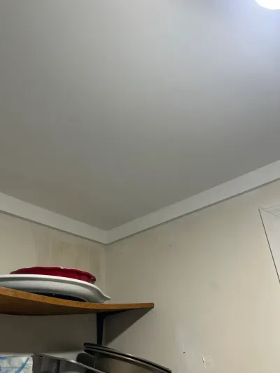 Upward view of a kitchen ceiling corner with crown molding and a wire shelf holding stacked cookware.