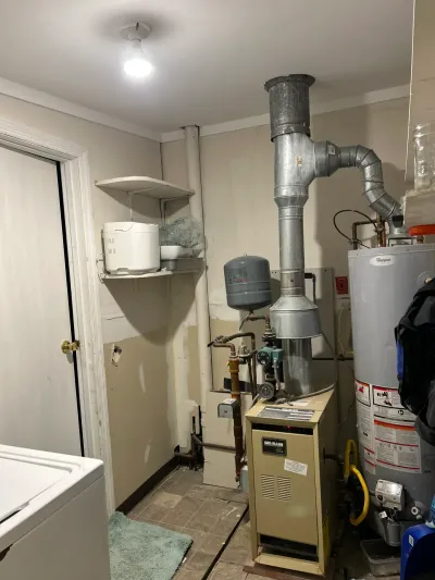Basement utility room with an aging boiler, water heater, and exposed pipework before renovation.