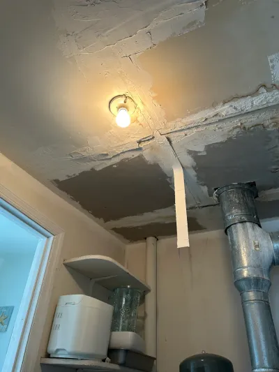 Ceiling drywall patch work in progress above ductwork and a storage shelf in a utility room.