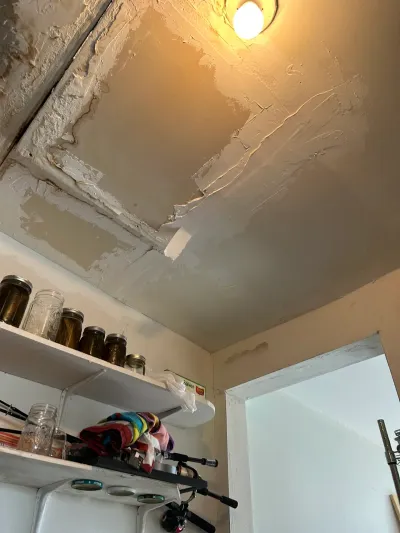 Ceiling drywall patch mid-repair above shelving stocked with canning jars in a basement room.