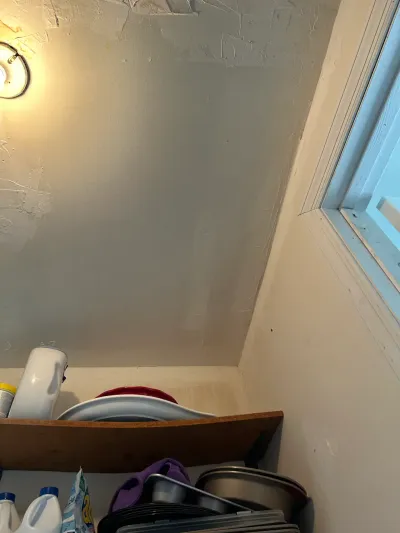 Sloped basement ceiling with patched drywall above open shelving stocked with household items.