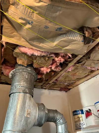 Exposed basement ceiling with torn insulation, a galvanized duct, and string lines marking layout during a remodel.