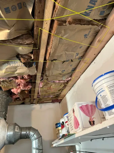 Open basement ceiling cavity with exposed insulation, wood joists, and ductwork during renovation work.