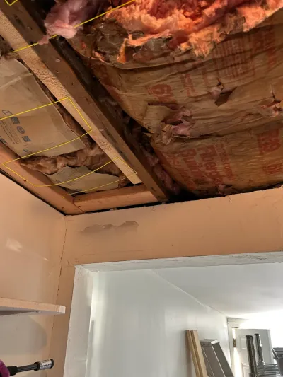 Exposed ceiling insulation and framing during a home renovation, with an open doorway to another room.