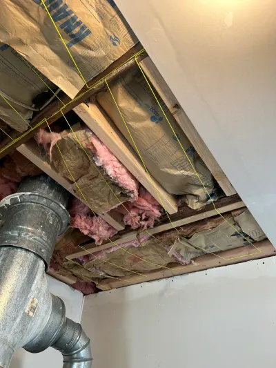 Open basement ceiling cavity showing insulation, framing, and ductwork with measurement lines marked.