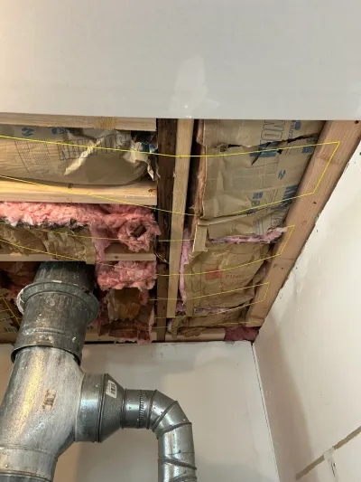Opened basement ceiling exposing insulation, framing, and ductwork with yellow markup lines highlighting an area.