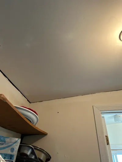 Kitchen ceiling corner with visible seam crack above an open shelf stacked with dishes.