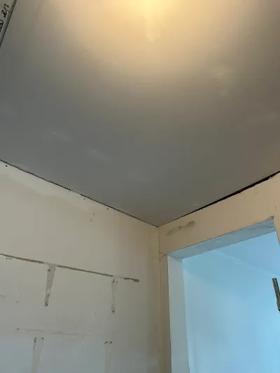 Unfinished drywall corner with visible patching compound next to a doorway leading to another room.