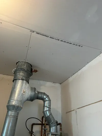 Unfinished basement ceiling and wall with fresh drywall and a galvanized vent pipe running through it.