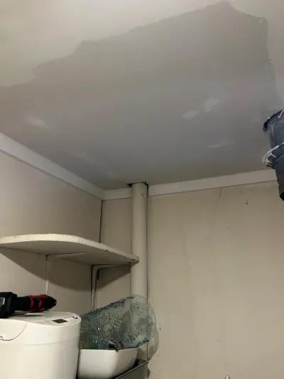 Ceiling drywall patch in progress above a storage shelf in a small utility closet.