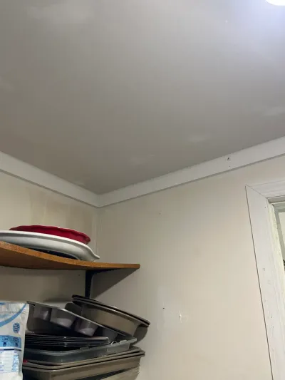 Corner of a pantry closet with open shelving stacked with bakeware, seen before renovation work.