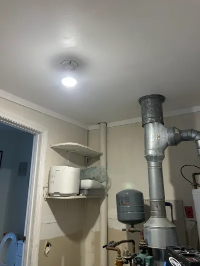 Utility room with exposed ductwork, piping, and patched drywall near a doorway to a bathroom.