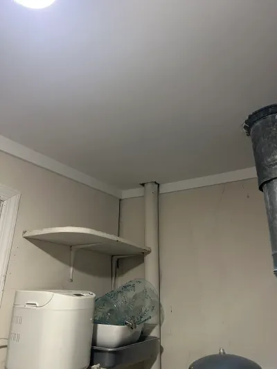 Unfinished basement corner with exposed ductwork, a wall shelf, and household appliances on the floor.