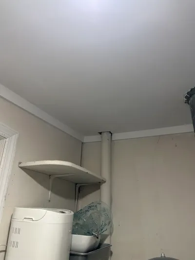 Corner of an unfinished basement room with a pipe, wall shelf, and stored kitchen appliances.