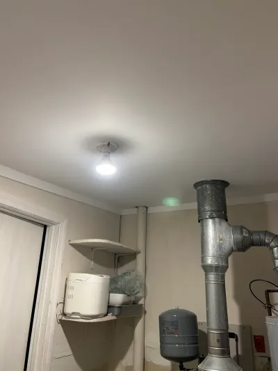 Basement utility area mid-renovation with exposed vent pipe, bare bulb light, and storage shelf.