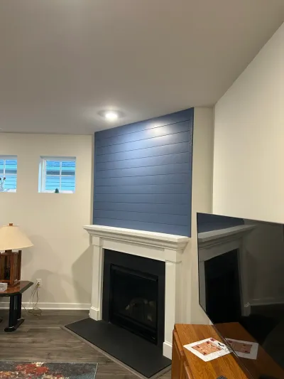 Finished basement with a white fireplace mantel, black tile hearth, and navy blue shiplap accent wall.